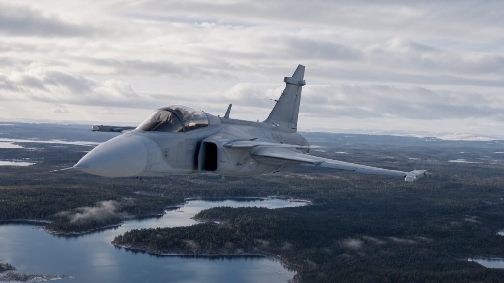 北欧の森林と湖上空を飛行するJAS 39グリペン級戦闘機