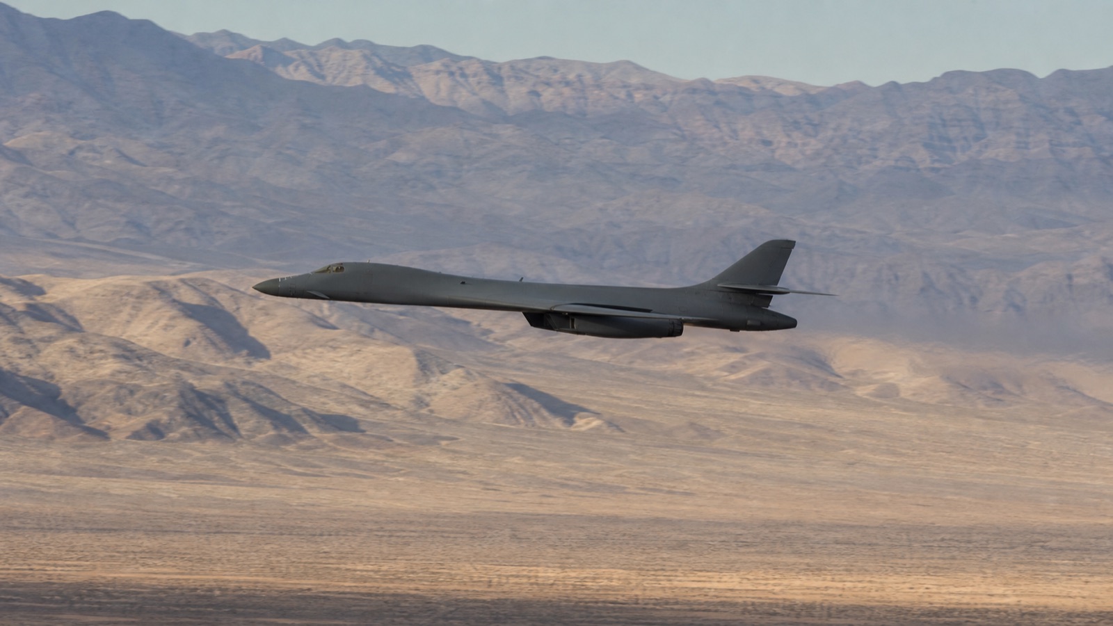 砂漠の山岳地帯を低空飛行するB-1B級可変翼爆撃機