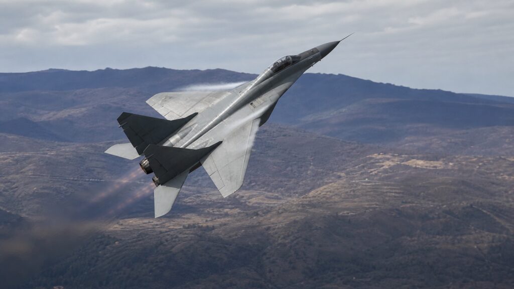 山岳地帯上空で上昇旋回するMiG-29級双発戦闘機