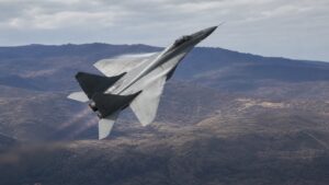 山岳地帯上空で上昇旋回するMiG-29級双発戦闘機