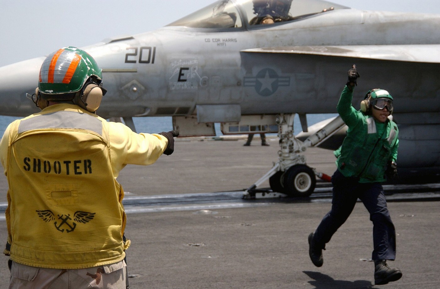 F/A-18Fの発艦準備。黄色と緑色のシャツの乗員が甲板で作業する。